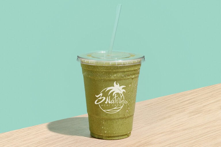 Green healthy smoothie in a takeaway cup from 3 Natives Acai Cafe on a pastel green background.