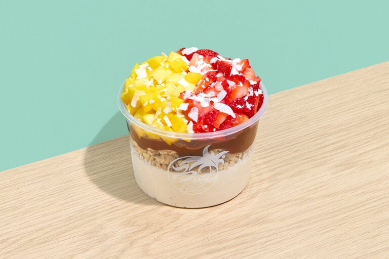 Creamy smoothie bowl topped with strawberries, pineapple, granola, chocolate drizzle, and coconut flakes