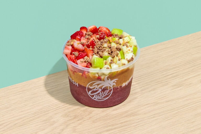 Açaí bowl with granola, peanut butter, strawberries, green apple, honey, and chocolate almonds in a clear serving cup