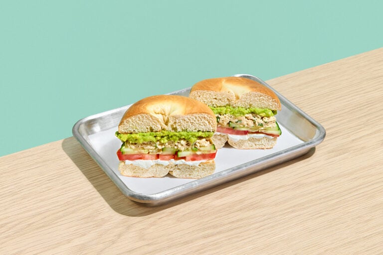 Mission Beach bagel sandwich with tuna salad, avocado, cucumber, tomato, and cream cheese on a silver tray.