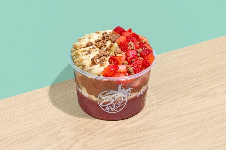 Acai bowl topped with banana slices, strawberries, chocolate drizzle, granola, and cookie crumbles