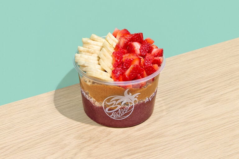 Açaí bowl with granola, peanut butter, banana slices, and fresh strawberries in a clear cup”