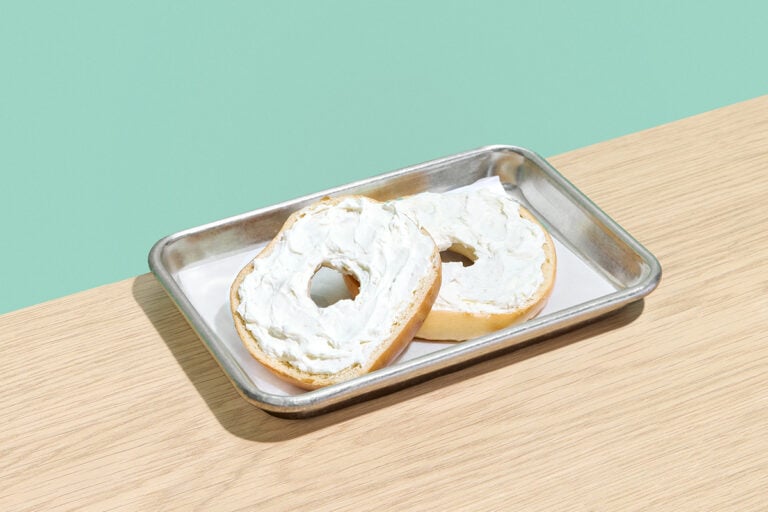 Plain bagel with cream cheese served open-face on a silver tray.
