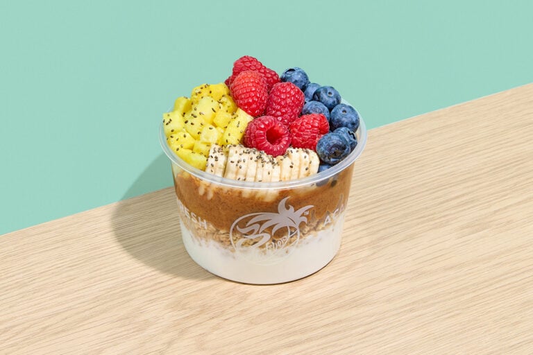 A Calypso fruit bowl layered with yogurt, granola, and almond butter, topped with fresh raspberries, blueberries, pineapple, and sliced bananas with chia seeds.