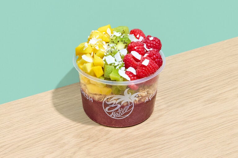 Açaí bowl with granola, raspberries, mango, kiwi, hemp seeds, and coconut shavings in a clear cup
